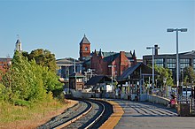 A curved railway platform with various buildings behind