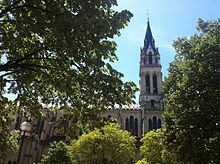 Photographie d'une église néo-gothique, vue du côté gauche (nord), au milieu des arbres d'un square.