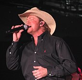 A man in a black shirt and cowboy hat, singing into a microphone