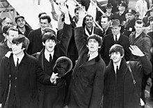 Greyscale image of the Beatles, wearing coats and waving their hands