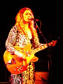 Julia Deans performing on stage, holding a guitar, lit in yellow