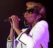 Mary J. Blige singing into a microphone on a stand with sunglasses on