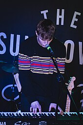 Sam Fender playing the piano with a striped black sweater