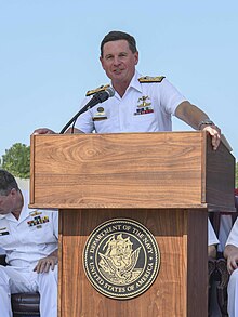 Colour photo of a man wearing a white uniform standing behind a lectern