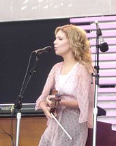 A woman wearing a pink dress and playing a fiddle.