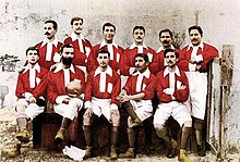 Eleven male footballers wearing red and white shirts with white shorts pose for a picture.