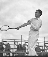A man in a white clothing with a wooden tennis racket