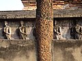 Colonne en pilier en latérite. Derrière, frise en briques avec des disciples de Bouddha.