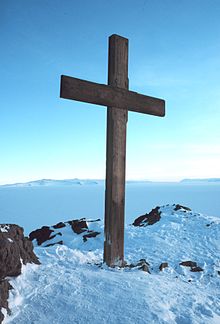 Flat-topped hill with snow on lower slopes and sea in the foreground, and a solitary bird in flight