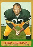 A color photo of Fuzzy Thurston crouching down looking towards the camera. The text "Fred Thurston, Green Bay Packers, Guard" is printed below the photo.