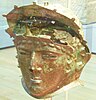 A corroded golden coloured helmet with a face shape to cover the wearer's face