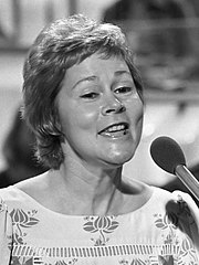 A black-and-white image of a woman with short hair singing into a microphone.