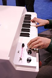 Photo d'un clavier électronique dont joue une personne dont seules les mains sont visibles, la droite sur les touches et la gauche ajustant un bouton