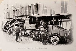 Photo noir et blanc d'un véhicule automobile en tête d'un convoi de fourgons.]]