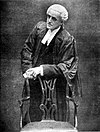 Photograph of a man leaning on a chair
