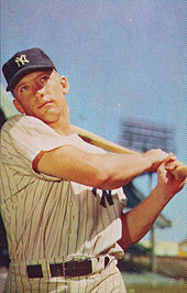 Medium-wide shot of baseball player Mickey Mantle, swinging a bat and wearing a "NY" shirt and hat.