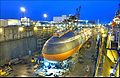 Photograph of the strategic missile submarine USS Ohio in drydock at the Puget Sound Naval Shipyard as night falls. The ship is surrounded by scaffolding and equipment, and several shipyard buildings appear in the background.