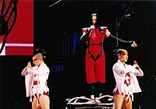 Madonna in a red dress, flanked by her dancers wearing white dress