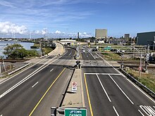 A six-lane urban highway with a railroad grade crossing under a blue sky.