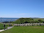 Grass-covered house surrounded by a fence, sea in the distance