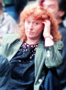 Red-headed woman in a green jacket and blue lace top