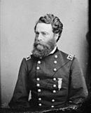 Black and white photo shows a heavily bearded man wearing a dark military uniform with two rows of buttons. The two stars on his shoulder tabs indicate a major general.