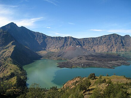 A small cone rising above a greenish lake within a large crater on a mountain