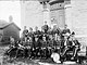 Black and white photograph of band members in uniform on front steps of stone township hall in 1894