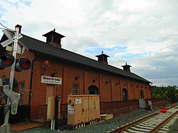 A one story brick building with a slanted roof adjacent to railroad tracks. Above the building's door is a sign reading "Windsor Art Center at the Freight House".