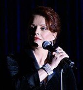 A brown-haired woman standing at a microphone and looking to her right