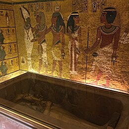 A coffin in a glass-lidded sarcophagus, in a room with painted walls