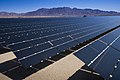 long rows of dark panels, sloped about 45 degrees at the height of a person, stretch into the distance in bright sunshine (from Sustainable energy)