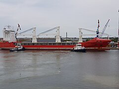 Un vraquier à quai flanqué de deux remorqueurs.