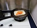 A makeshift steaming vessel with lid removed; a frozen dish is placed on a metal frame in a single handled wok with water.