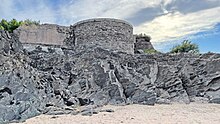 A stone platform, previously the site of a gun battery, located on top of a low cliff and seen from the beach below the cliff.