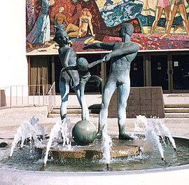 Bronze sculpture of dancing family, above burbling fountain, mosaic mural in background