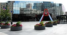 A color photograph of an office building. A pyramid-shaped sculpture stands in front of it.