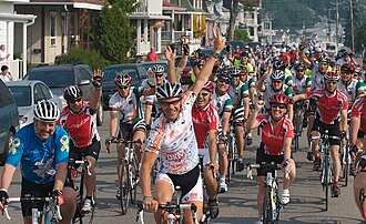 Peloton de coureurs cyclistes, vu de face. L'homme devant lève son bras gauche.