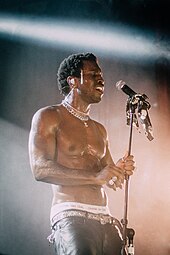 A picture of Saint Jhn during a concert, singing shirtless into a microphone.