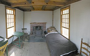 L'intérieur de la cabane de Thoreau. Au fond et au centre : une cheminée de briques rouges à côté de laquelle est une caisse de bois de chauffe et à droite et à gauche : deux fenêtres. À droite, un lit fait ; à gauche, une chaise et une petite table ronde. On aperçoit sur le côté gauche, au premier plan, une partie d'un secrétaire pour écrire.