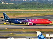 A plane that is painted in red in the front and navy blue in the back, with a red-to-blue ombre in the middle, a navy blue eskimo on the tail, and the words "MORE TO LOVE" across the fuselage, is taxiing on an airport taxiway