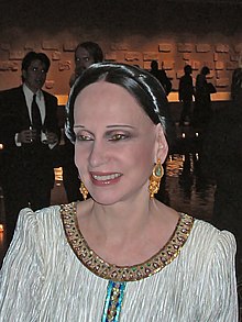 Headshot of McFadden in white clothes adorned with jewelry in a dark setting