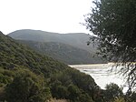 A view of two large hills and a small beach, partially obstructed from the left by a larger vegetated hill.