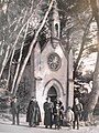 Plusieurs personnes dont un prêtre catholique en habit liturgique devant la chapelle du Plantier, entourée de grands pins.