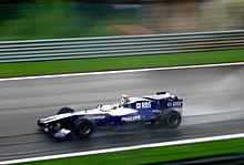 A dark blue and white Formula One being driven at high speed on a racing circuit