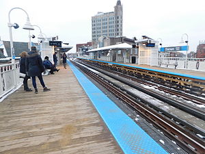A view down snowy railroad tracks surrounded by two wooden side platforms with blue tactile edging and white canopies