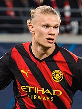 Erling Haaland wearing a red-and-black diagonally striped football jersey.