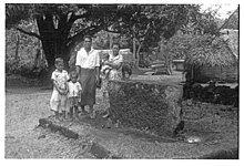 Photo en noir et blanc d'une famille composée d'un couple et trois enfants posant devant une large pierre rectangulaire