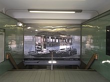 Interior of a subway entrance, with a mural of a streetcar on a reflective panel
