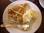 Treacle tarts are prepared using shortcrust pastry, with a thick filling made of golden syrup, also known as light treacle, breadcrumbs, and lemon juice or zest. Pictured is a treacle tart with clotted cream.